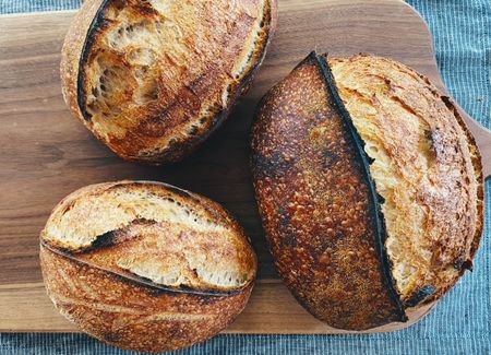 Three beautiful loaves of sourdough arranged haphazardly on a wooden cutting board.
