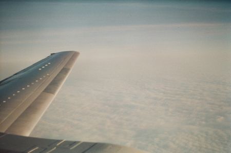 View from an airplane window. A layer of clouds spread out below the wing.