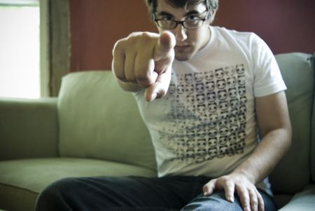 Joel Goodman pointing at the camera from a couch