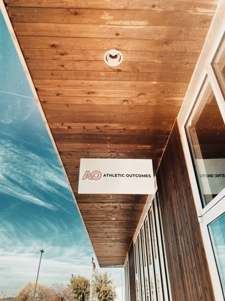The storefront of a gym with a branded sign hanging above that reads Athletic Outcomes.