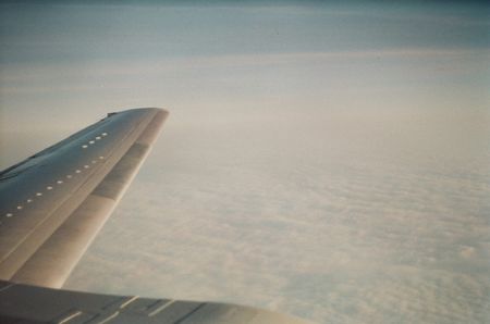 View from an airplane window. A layer of clouds spread out below the wing.
