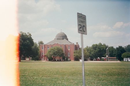 A 20 MPH speed limit sign on a country road with a church in the background.